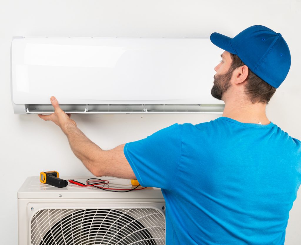 Installation service fix repair maintenance of an air conditioner indoor unit, by cryogenist technican worker in blue shirt baseball cap